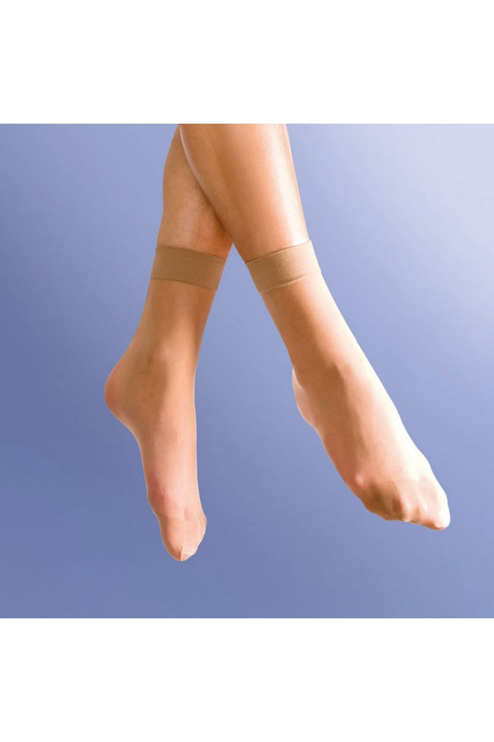 Close-up of legs wearing smooth knit natural tan anklets against a light blue background