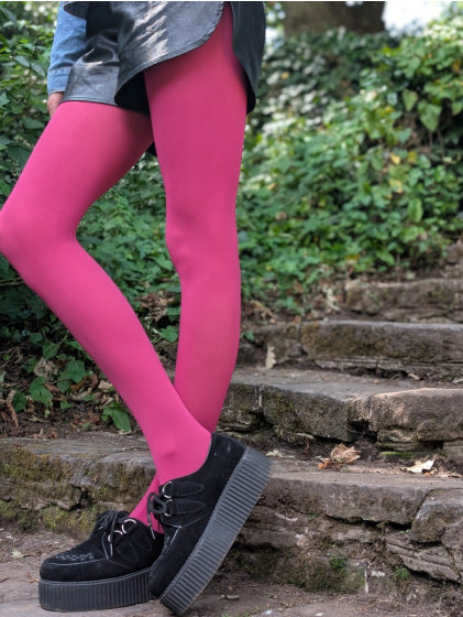 Person wearing bright pink pretty polly tights and black shoes on stone steps with greenery in the background