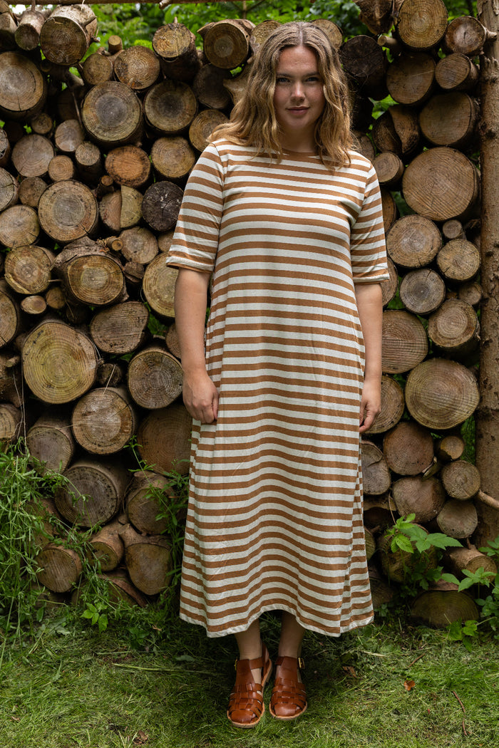 Woman wearing a striped dress standing in front of stacked logs.