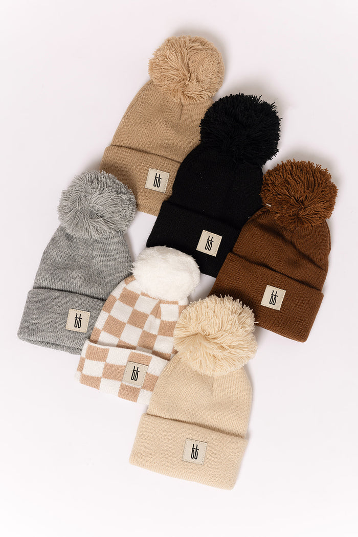 Six cozy ff Knit Pom Top Beanies from forever french baby—including the trendy Tan Checkerboard style—are arranged on a white background. Each features a folded brim and logo patch, perfect for keeping little ones stylish and warm.