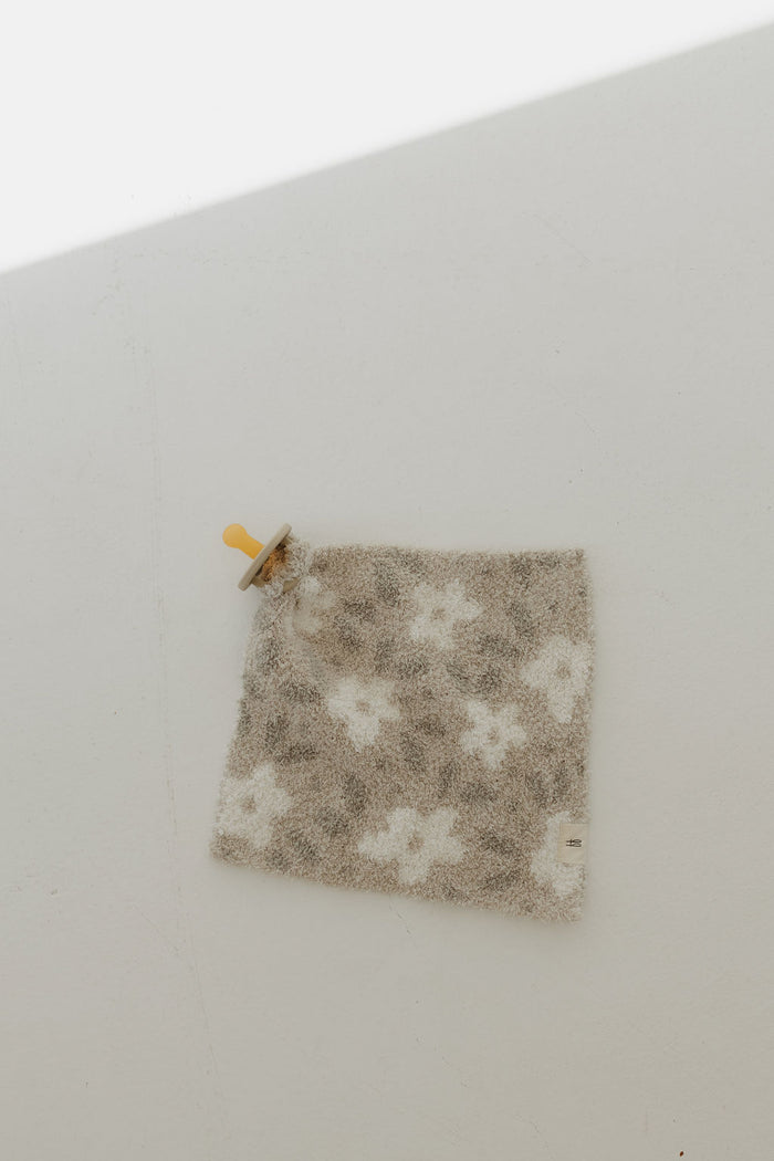 The Forever French Baby Lovey in a French Gray Floral print is displayed flat on a light surface. It features a wooden ring in one corner, potentially serving as a teether or grip, with soft shadows enhancing its elegance.