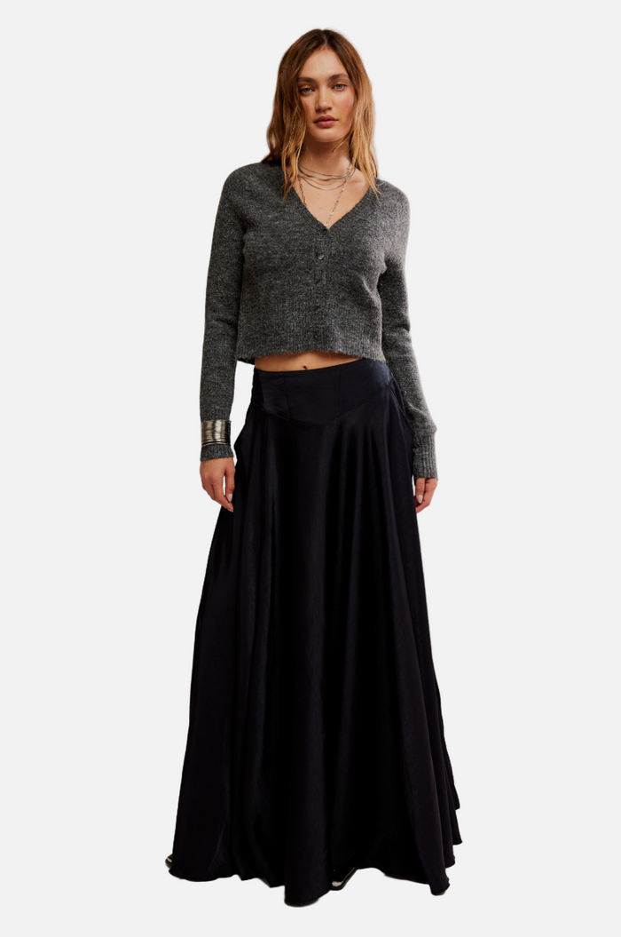 Woman wearing a gray cropped sweater and black long skirt on a plain background