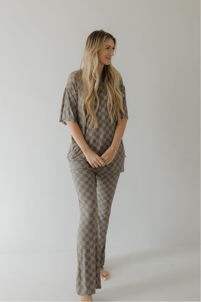 A barefoot woman with long blonde hair wears the forever french baby Short Sleeve Women's Bamboo Pajama in Faded Checkerboard, a stylish, hypo-allergenic set perfect for minimalist spaces.