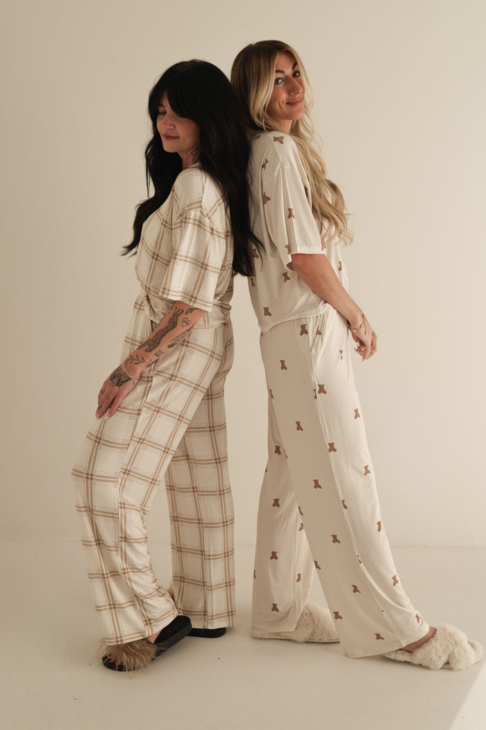 Two women stand back to back, smiling in Women's Boxy Tee Lounge Sets by forever french baby. One wears plaid with dark slippers, the other a small print with light slippers. Their soft bamboo sets are hypo-allergenic, shown on a plain background.