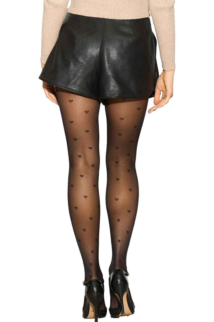 Model wearing black leather shorts and heart-patterned tights on a white background