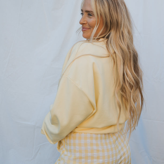 A woman with long blonde hair smiles over her shoulder in a forever french baby Adult Sweatshirt | ff Yellow against a white background—perfect for relaxed, everyday wear.