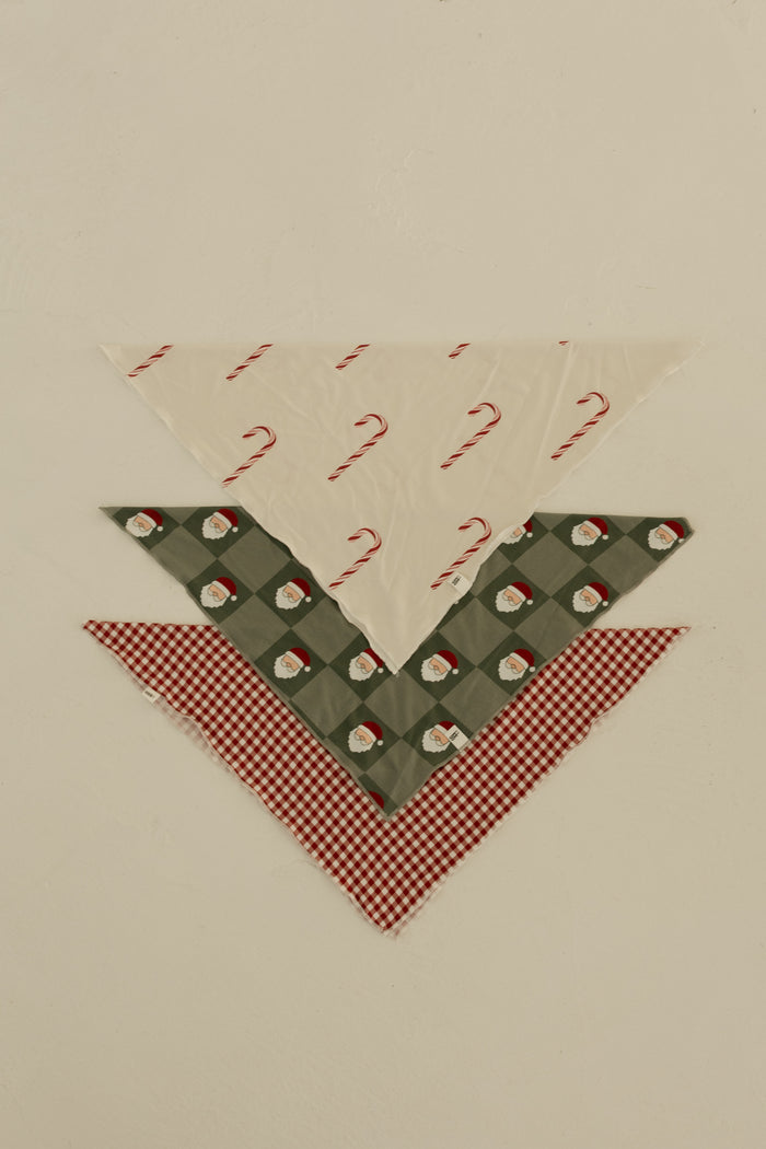 Three Bamboo Bandanas by forever french baby are stacked: candy cane print on top, Santa faces on green plaid in the middle, and red and white gingham on the bottom—perfect for a festive look!.