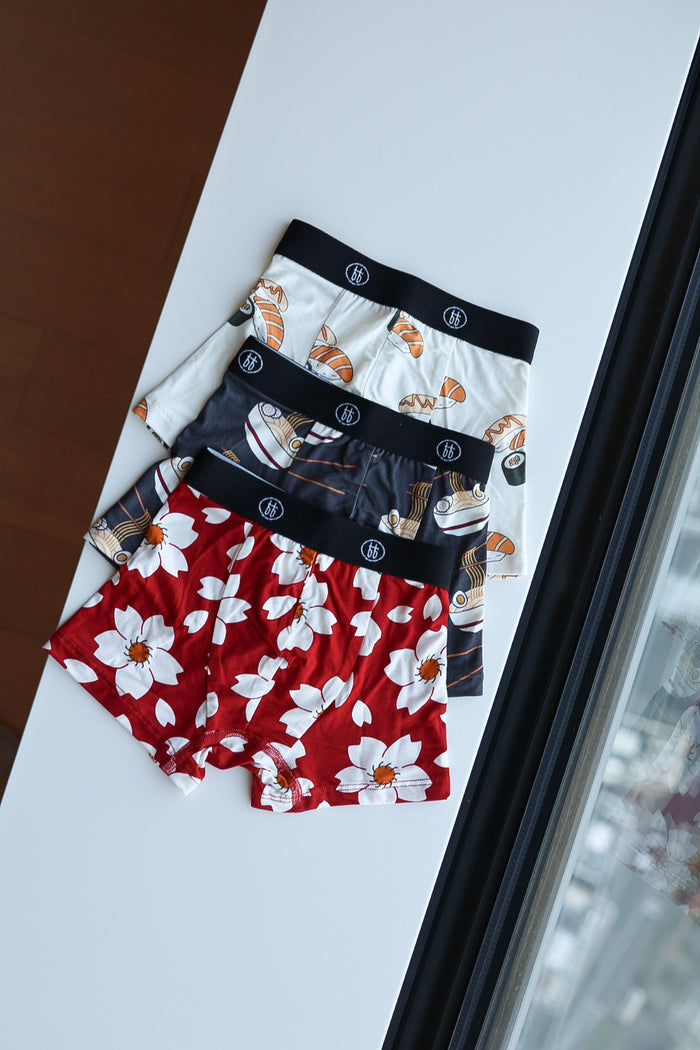 Three pairs of forever french baby Bamboo Boxers (3 Pack)—featuring Cherry Blossoms, Ramen, and Sushi patterns—are neatly folded on a white surface by a window.