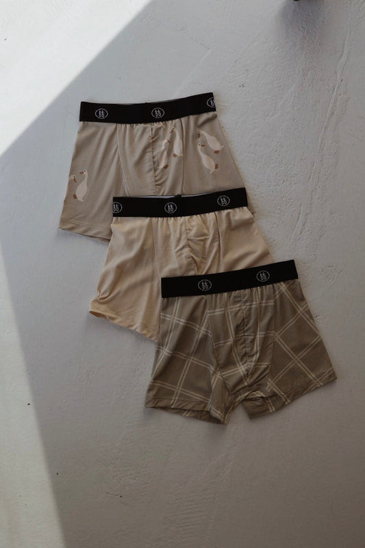 Three pairs of forever french baby Bamboo Boxers (Silly Goose, Bone & Linen Grid) are displayed on a white surface, featuring a polar bear print, plain beige, and a beige grid pattern. Hypoallergenic comfort included.