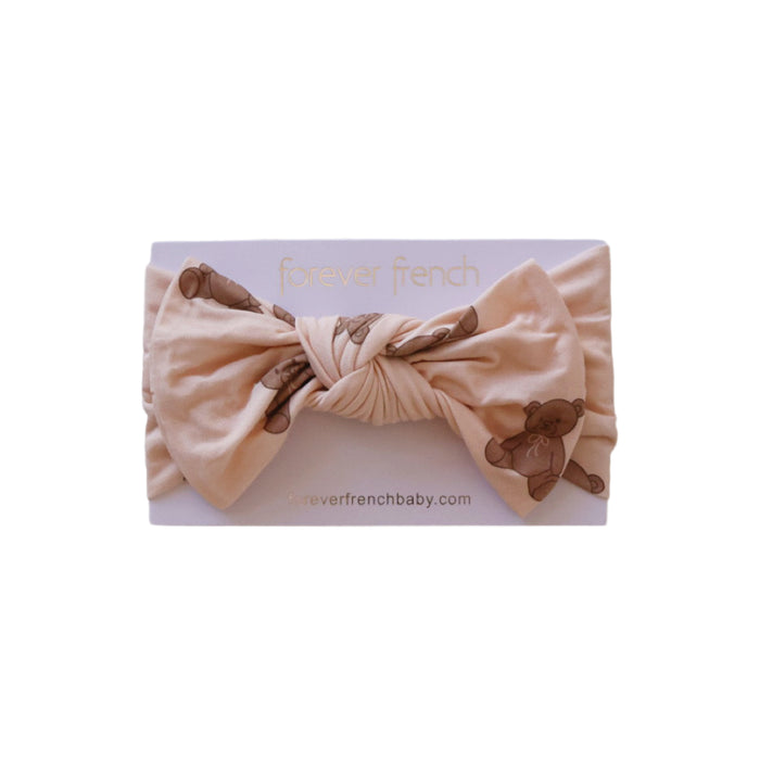 The Bamboo Head Wrap | Lottie by forever french baby is a soft beige baby headband featuring a large bow and brown teddy bear print, displayed on a branded card.