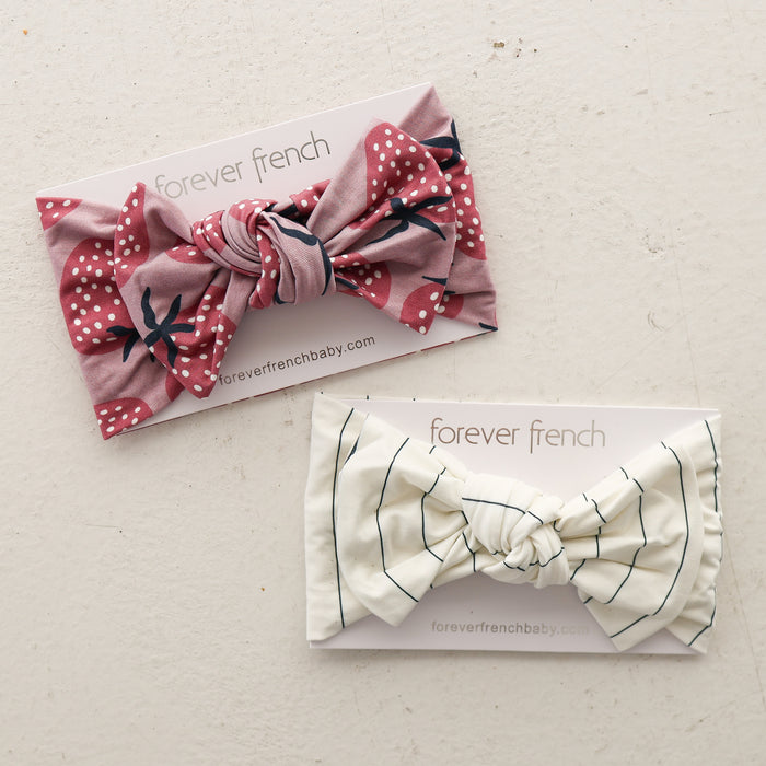 Two Bamboo Head Wrap | Matilda headbands by forever french baby are shown on branded cards: one is pink with white polka dots and florals, the other cream with thin black stripes, all on a light, textured surface.