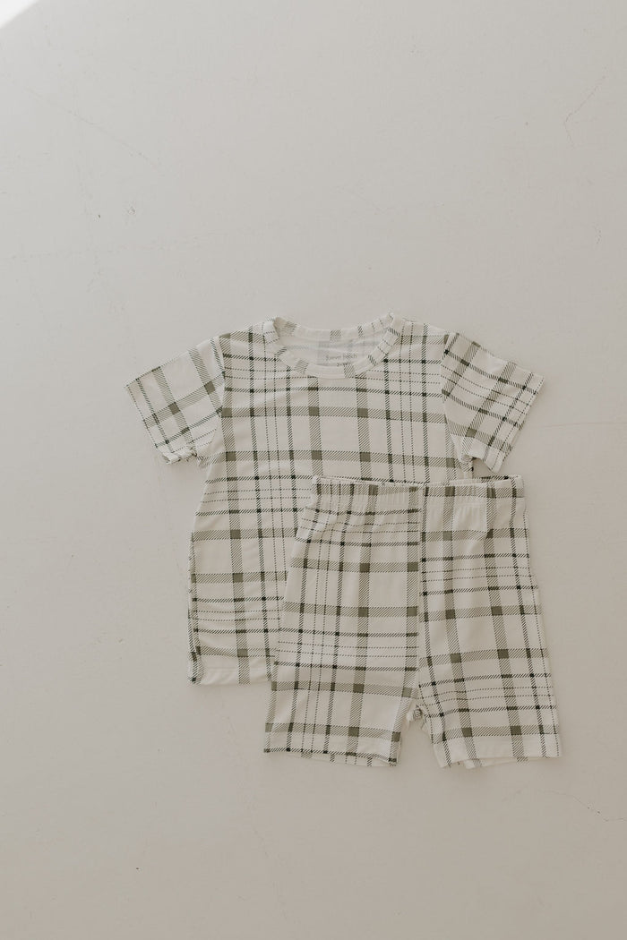 The Bamboo Short Set | Picnic Plaid by forever french baby is a children's pajama set featuring light and dark green plaid on a white background, made from breathable fabric. The set includes a short-sleeve top and matching shorts, displayed flat on a plain light surface.