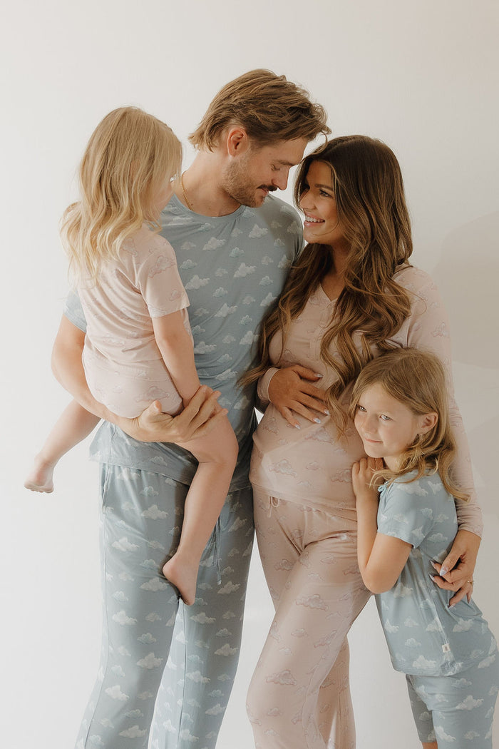 A smiling family of four wears matching Kendy 3 "Bamboo Short Set | Ruby" pajamas, featuring hypo-allergenic comfort and stylish cloud patterns as the father holds one child and the mother hugs the other.