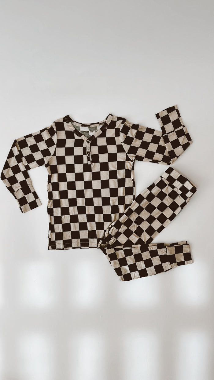 Laid flat on a white surface, the Black Checkerboard Bamboo Two Piece Pajamas by forever french baby feature a long-sleeve shirt with a partial zipper at the collar and matching pants. These cozy pajamas offer both style and comfort for your little one.
