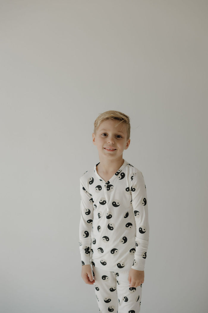 A young boy smiles at the camera in forever French baby's Bamboo Two Piece Pajamas | Black & White Yin Yang—hypoallergenic and perfect for sensitive skin, against a plain light gray background.