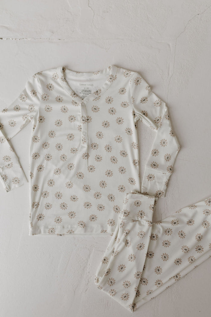 The Daisy Fields Bamboo Two Piece Pajamas by forever french baby features a floral pattern with a breathable, white bamboo long-sleeved button-up top and matching pants, showcased on a light textured surface.