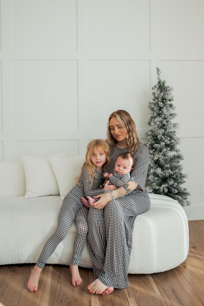 A woman and two young children in forever french baby’s Bamboo Two Piece Pajamas | Green Gingham relax on a white sofa by a festive tree, showcasing cozy, breathable holiday sleepwear for kids.