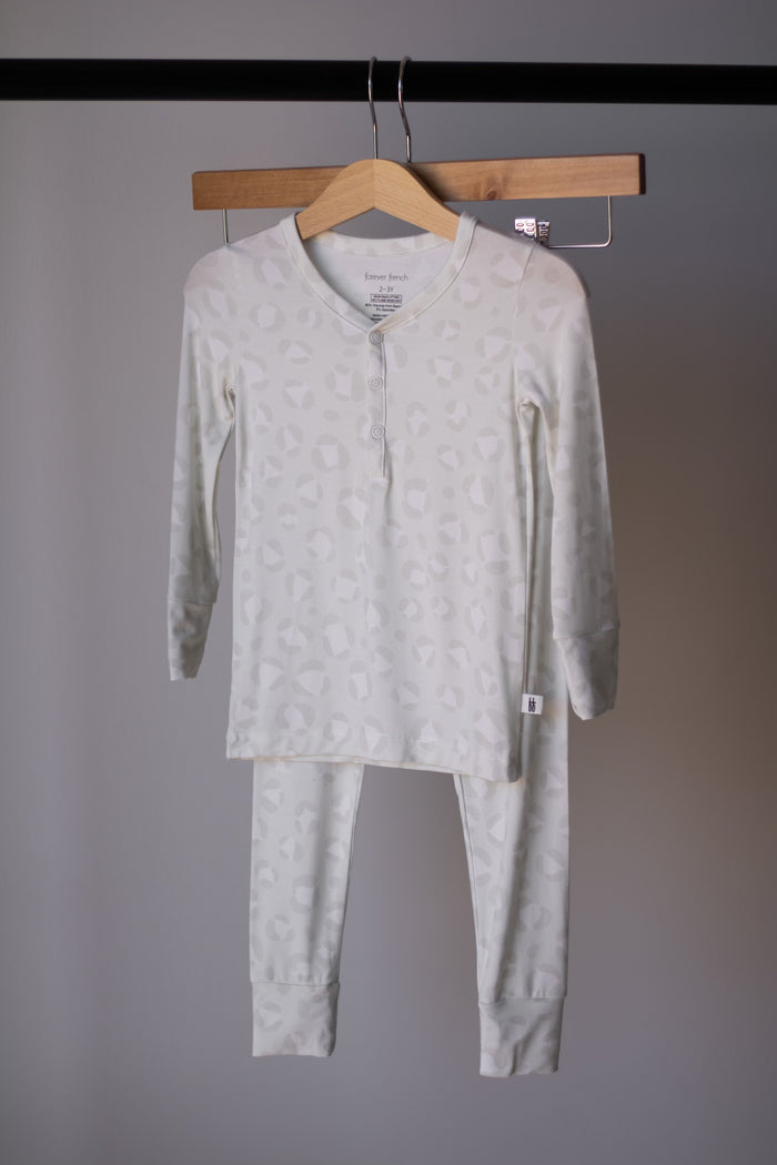 The Bamboo Two Piece Pajamas | Meow by forever french baby, featuring light-colored long sleeves and subtle geometric patterns, hangs on a wooden hanger against a plain background.