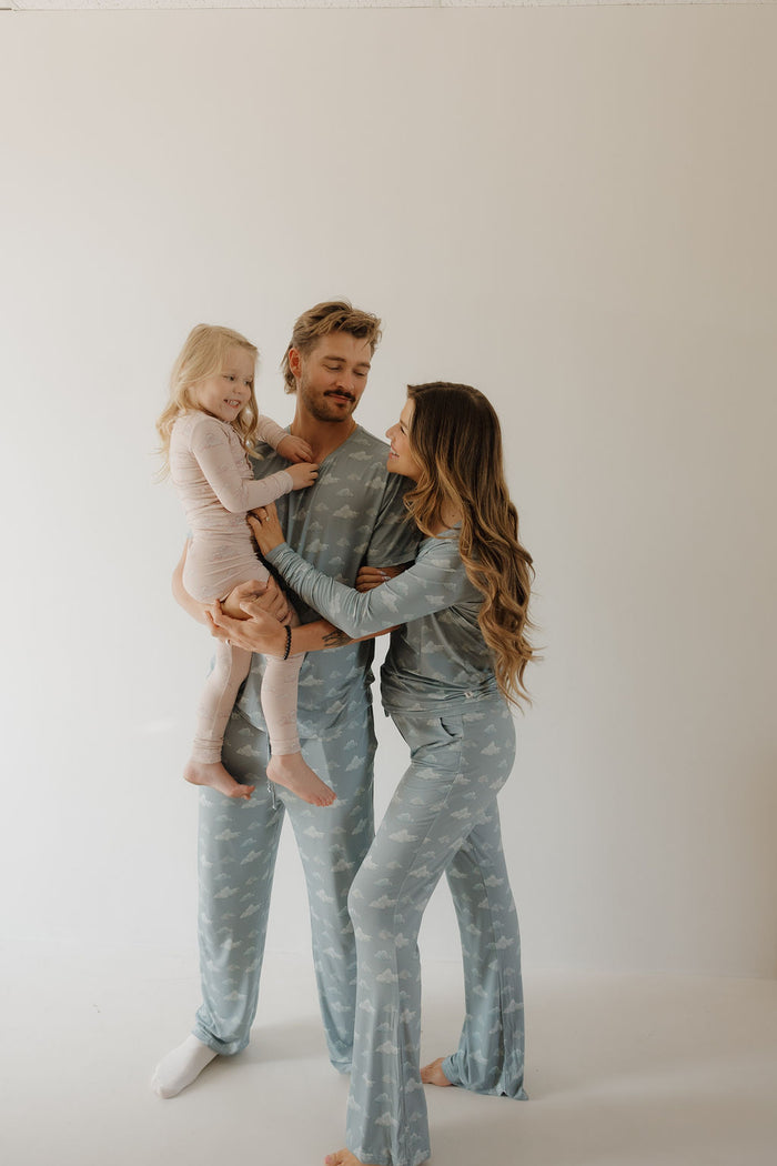 A smiling family in soft, breathable Kendy 3 Bamboo Two Piece Pajamas—parents in matching blue, daughter in light pink—stand together against a white background, radiating happiness and comfort.