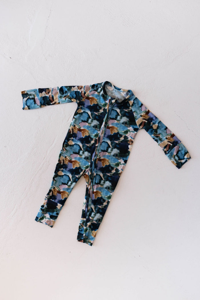 The Bamboo Zip Pajamas | Charli Print by forever french baby are displayed flat on a white background. This long-sleeve baby onesie features a front zipper and is crafted from soft bamboo fabric, adorned with a colorful abstract pattern in shades of blue, green, and brown. These baby pajamas offer comfort while promoting Autism awareness through their vibrant design.