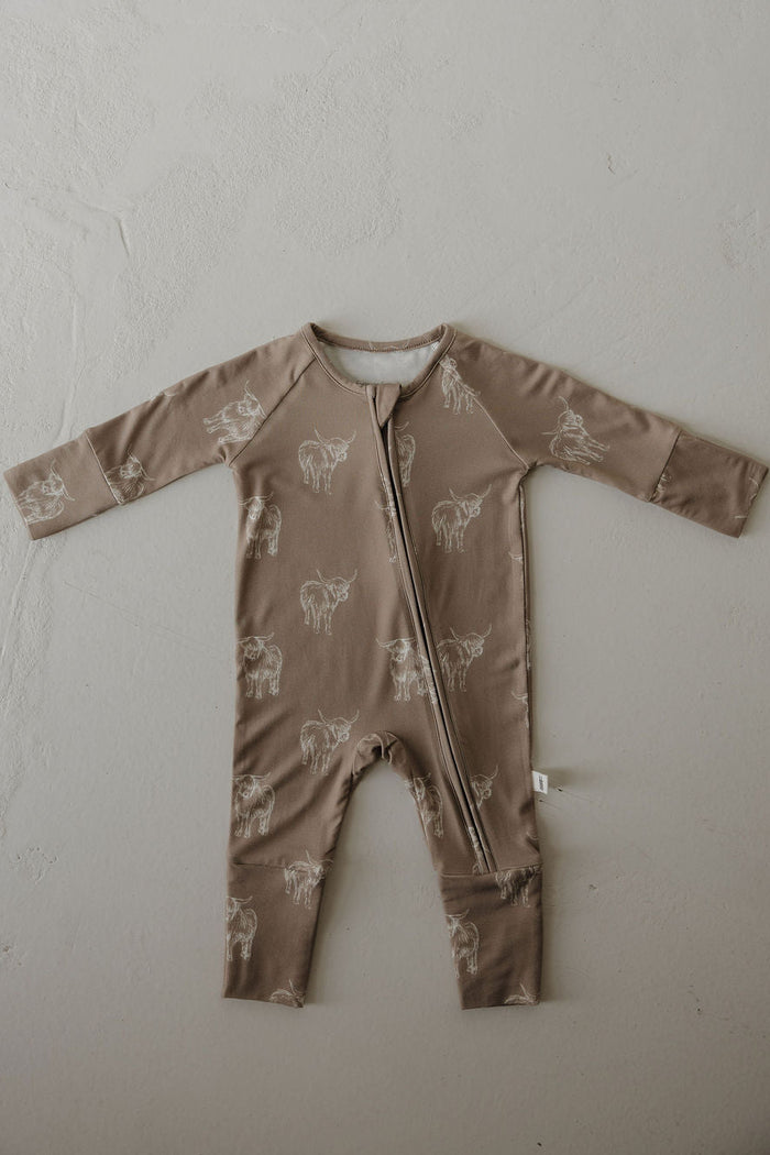 The Bamboo Zip Pajamas | Highland by forever french baby is a brown, long-sleeve romper made from breathable fabric with white animal sketches and a diagonal zipper, displayed flat on a light textured surface.