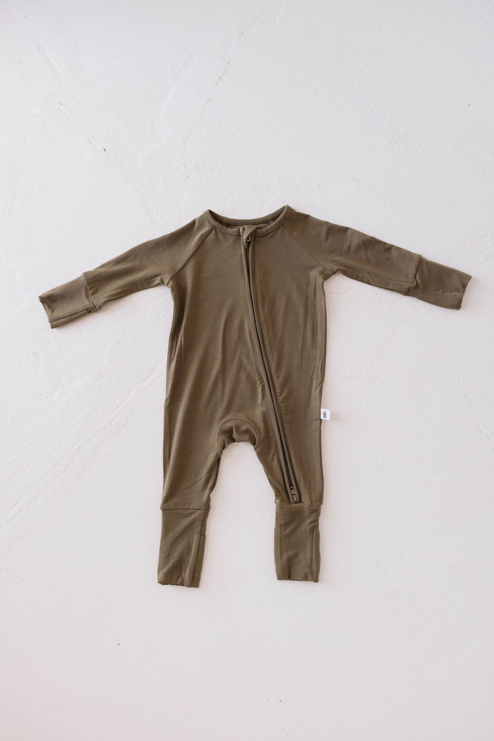The Bamboo Zip Pajamas in olive green from forever french baby feature a long-sleeve design made from premium bamboo. They have a diagonal zipper that extends from the neck to one ankle, showcased on a white, textured background. This garment's simple and minimalist style makes it perfect as Forever French Pajamas for your little one.