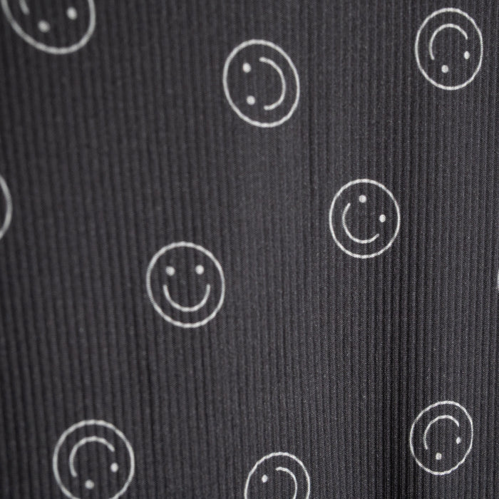 A close-up of the forever french baby Child Boxy Tee Lounge Set | Smiley Ribbed shows dark ribbed fabric with white outlined smiley faces, some full and some partial—perfectly spaced and ideal for comfy, breathable children's loungewear.