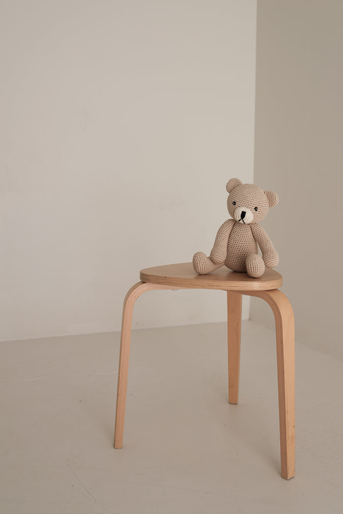Benson the Bear | Knit Doll by forever french baby rests on a simple wooden stool in a minimal, light-filled room.