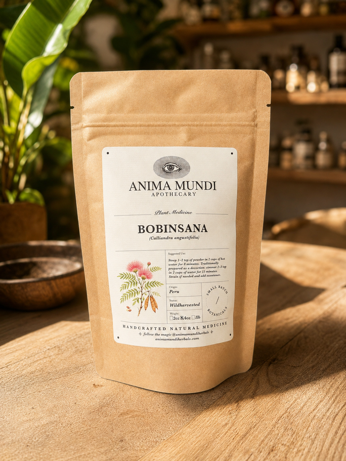 A kraft paper stand-up pouch of Anima Mundi Apothecary Bobinsana herbal remedy, standing on a wooden surface with a warm, softly blurred background of plants and shelves.