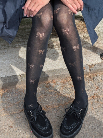 Black tights with bow pattern worn by a person on a stone pavement.