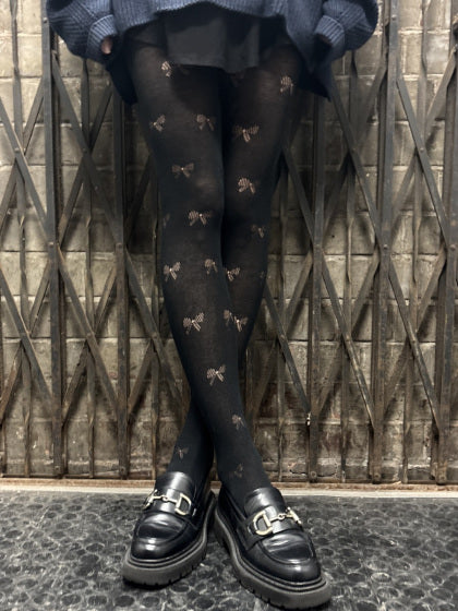 Person wearing pretty polly black tights with bow pattern and black shoes against a textured wall.