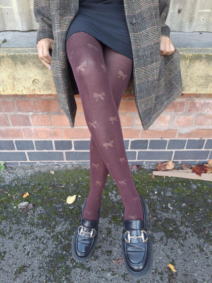 Person wearing pretty polly bow patterned tights and a coat standing against a brick wall.