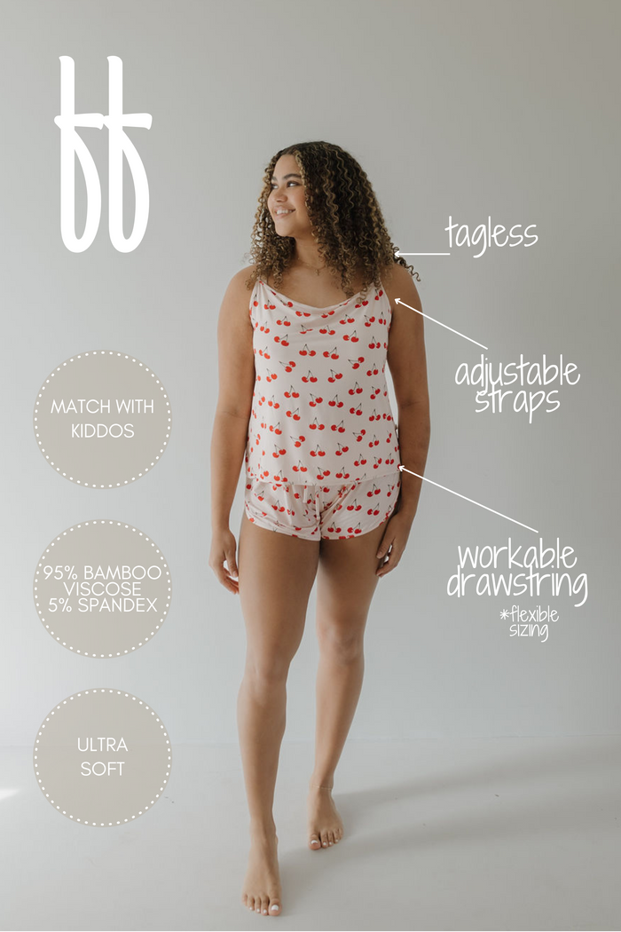 A woman smiles in the Cami Women's Bamboo Set | Cherry Orchard by forever french baby. This hypoallergenic set features tagless construction, adjustable straps, and a workable drawstring for flexible sizing. Made of 95% bamboo viscose and 5% spandex, it offers breathable comfort and matches kids' clothes.