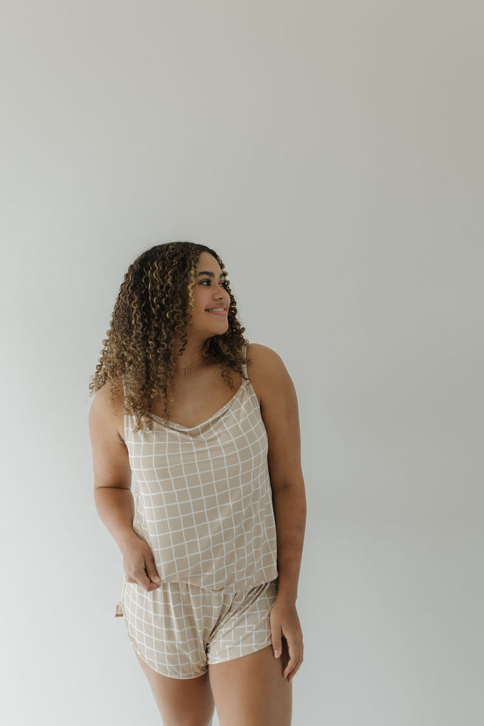 With a smile, a curly-haired person models the forever french baby Cami Women's Bamboo Set in a white grid pattern against a plain, light background.