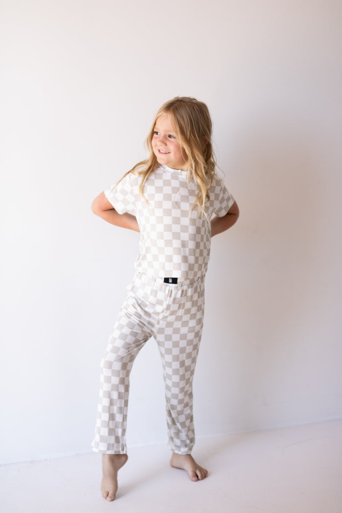 A young child with long blonde hair stands barefoot against a plain white background, smiling in breathable comfort while wearing the forever french baby Child Boxy Tee Lounge Set | Checkerboard.