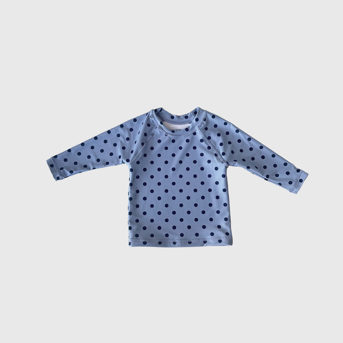 The Child Rash Guard | Sully by forever french baby is a light blue, long-sleeve kids’ swim top with dark blue polka dots for stylish sun protection, shown against a plain white background.