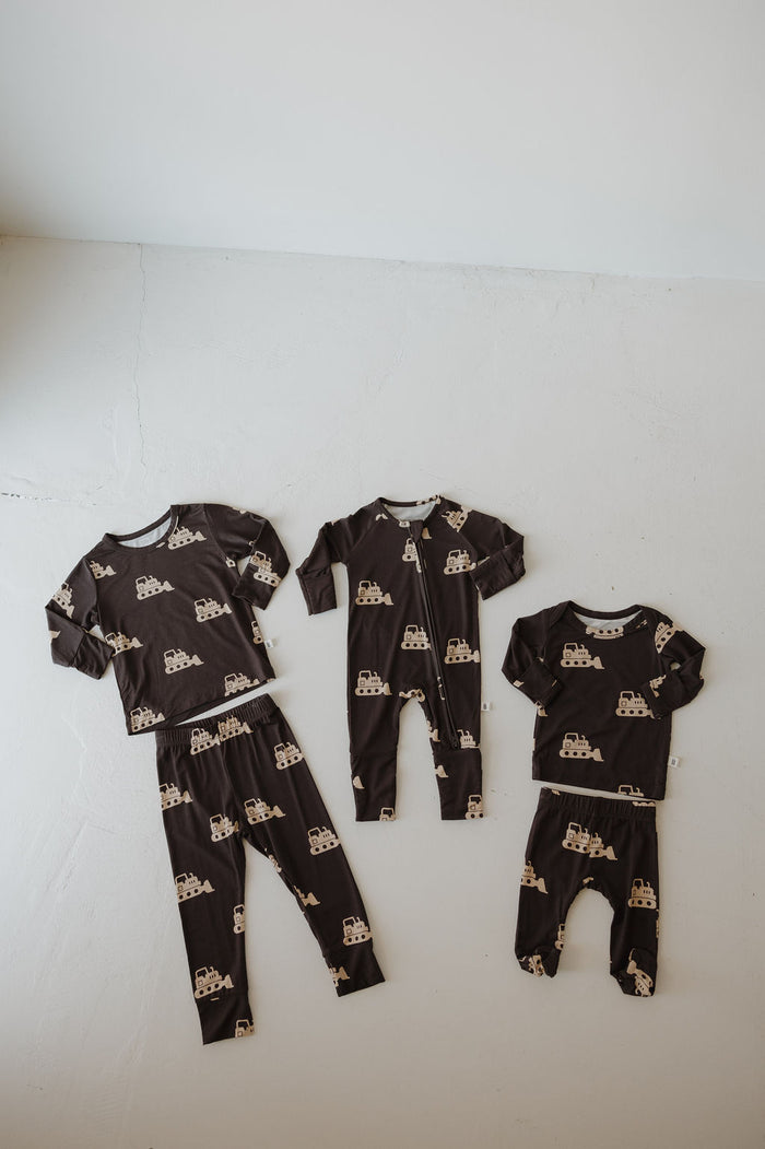 Four Child Sleepy Time Sets in the Bulldozer print by forever french baby, shown in matching dark brown bamboo fabric. Includes two long-sleeve and two short-sleeve pajama sets, all laid out on a light floor.