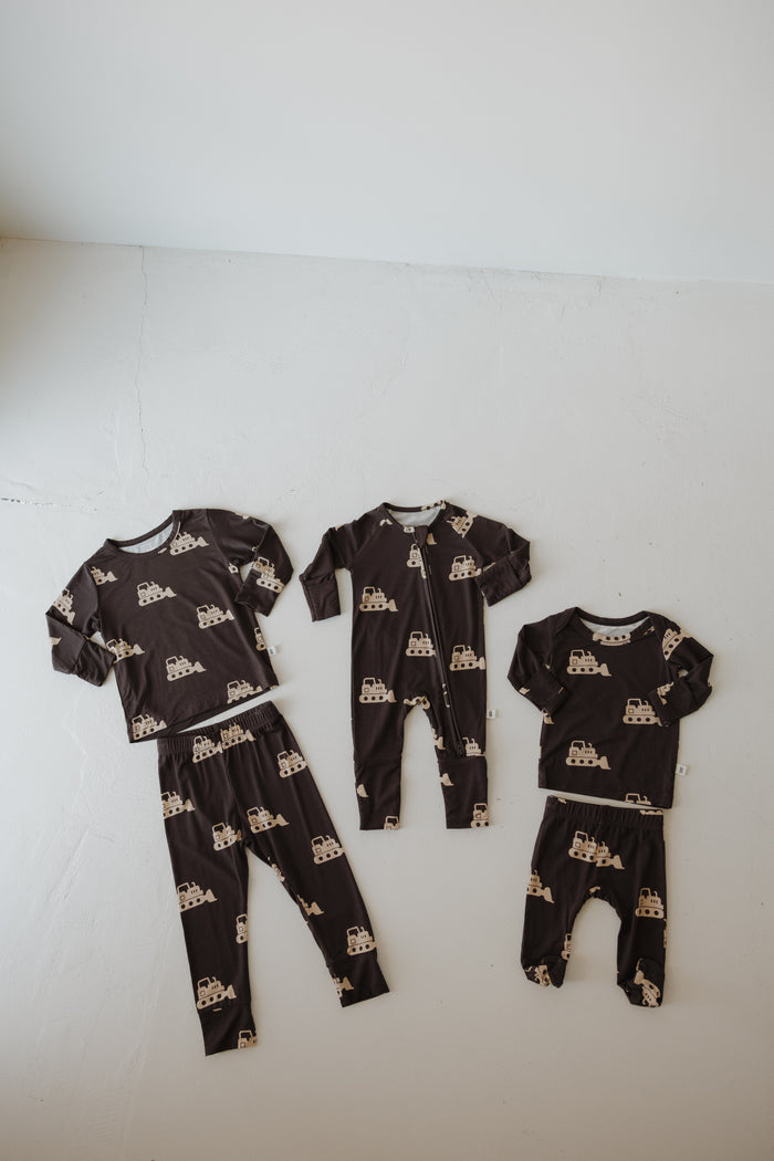 Four matching "Child Sleepy Time Set | Bulldozer" pajamas by forever french baby, made from breathable bamboo, are displayed on a light floor. The set includes two tops and pants sets plus two footed onesies in assorted sizes.