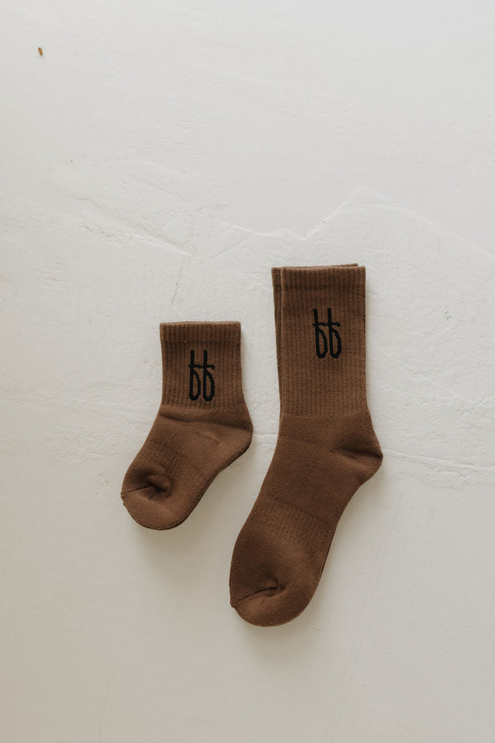 Two ff Crew Socks in Whiskey from forever french baby lie on a light surface, with the smaller sock on the left and the larger on the right, each adorned with black "bb" lettering—ideal for any family loving Forever French Baby style.