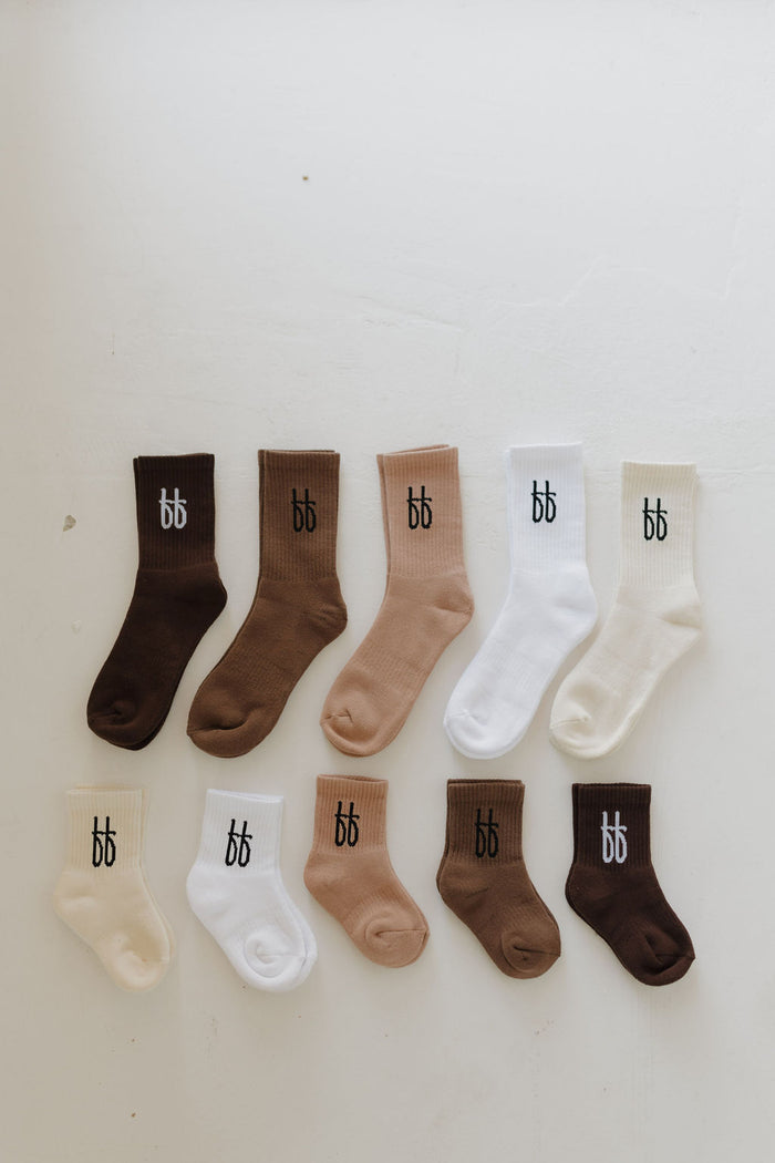 The ff Crew Socks | Cocoa by forever french baby are cozy crew socks in brown, cream, and white with a "bb" logo near the top. They're neatly arranged in two rows on a light surface and offer sizes for all family members.