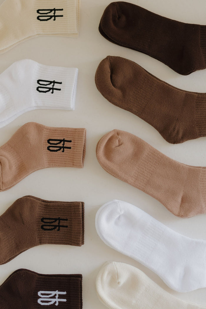 A variety of ff Crew Socks | Cocoa by forever french baby are displayed in rows on a light surface, featuring shades of brown, beige, and white. Each sock showcases a small logo near the top, exuding timeless elegance suitable for the entire family.