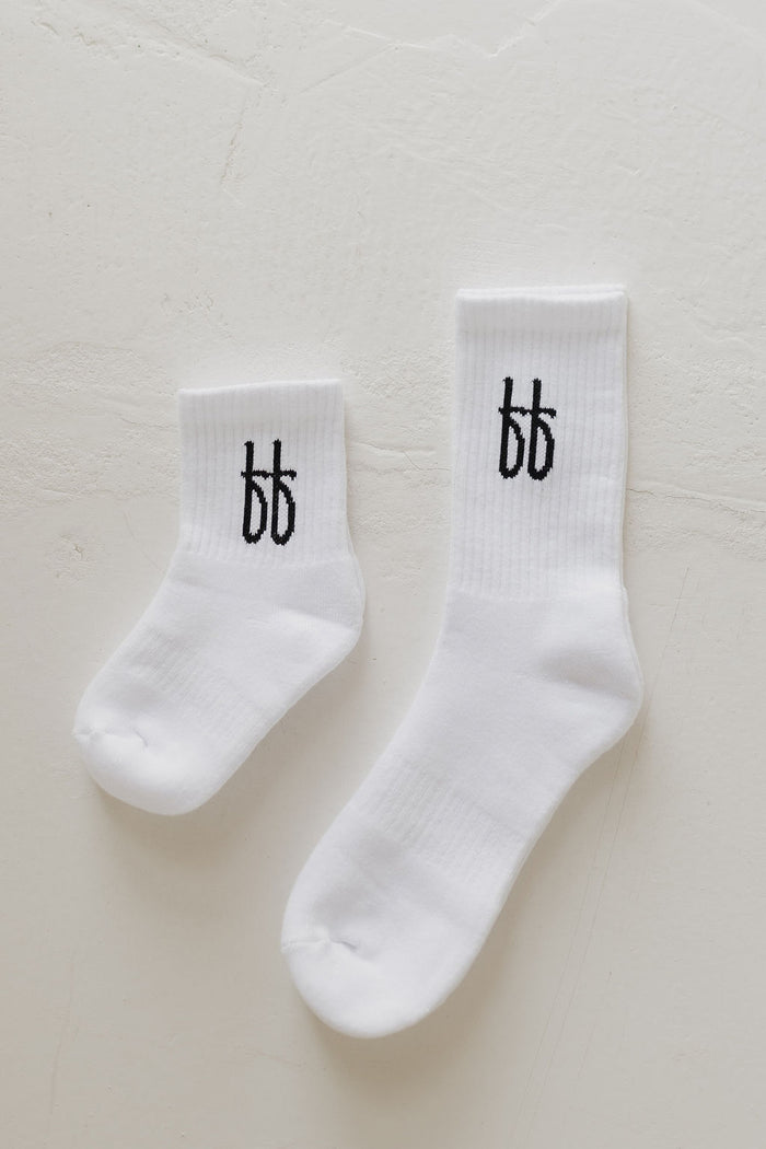 A comfy pair of white ff Crew Socks, by forever french baby, each featuring the black "bb" logo on the ankle and one slightly smaller than the other, displayed on a light textured surface—ideal for everyday wear.