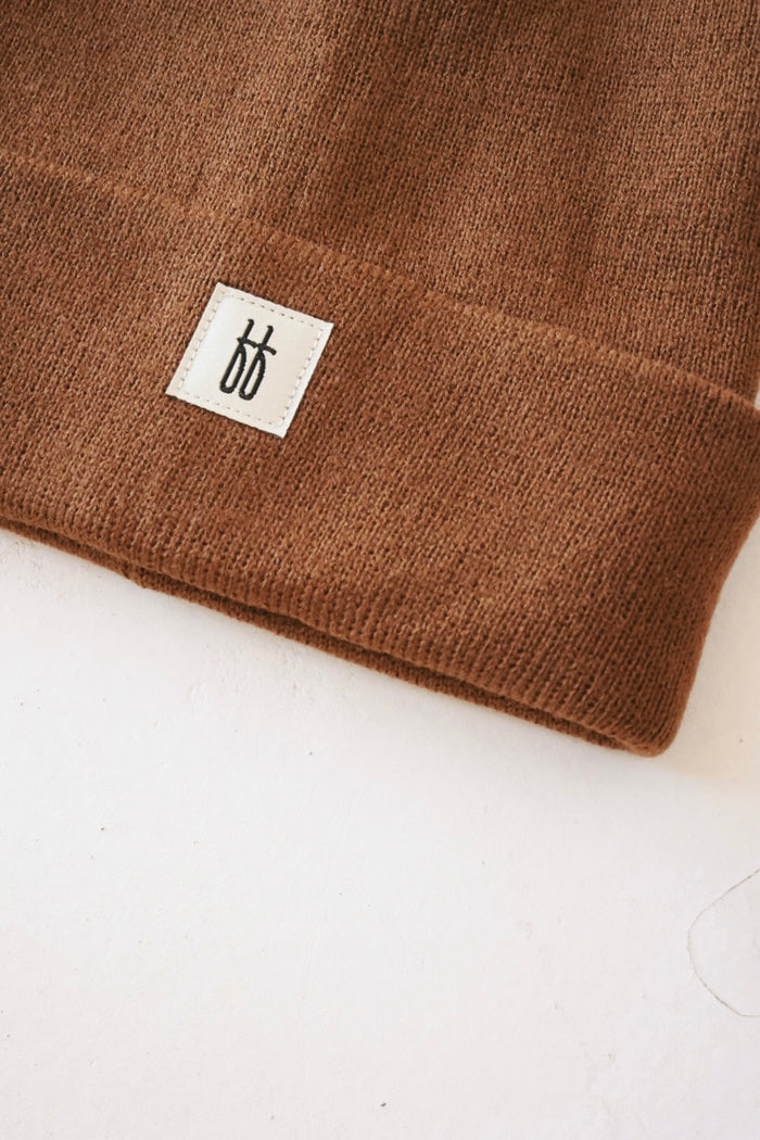 Close-up shot of a forever french baby ff Knit Beanie | Adult featuring a white rectangular tag with a minimalist black logo composed of two adjacent "b" shapes. The breathable yarn fabric appears soft and textured, with the image highlighting the ribbed design along the lower edge of the beanie.
