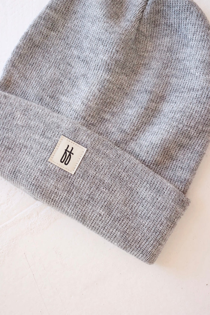 The forever french baby ff Knit Beanie | Adult is displayed on a white surface. With its ribbed design, this gray beanie features a folded brim adorned with a small, rectangular white label showcasing the brand's black stylized logo. The texture of the breathable yarn is visible, giving the beanie a cozy appearance.