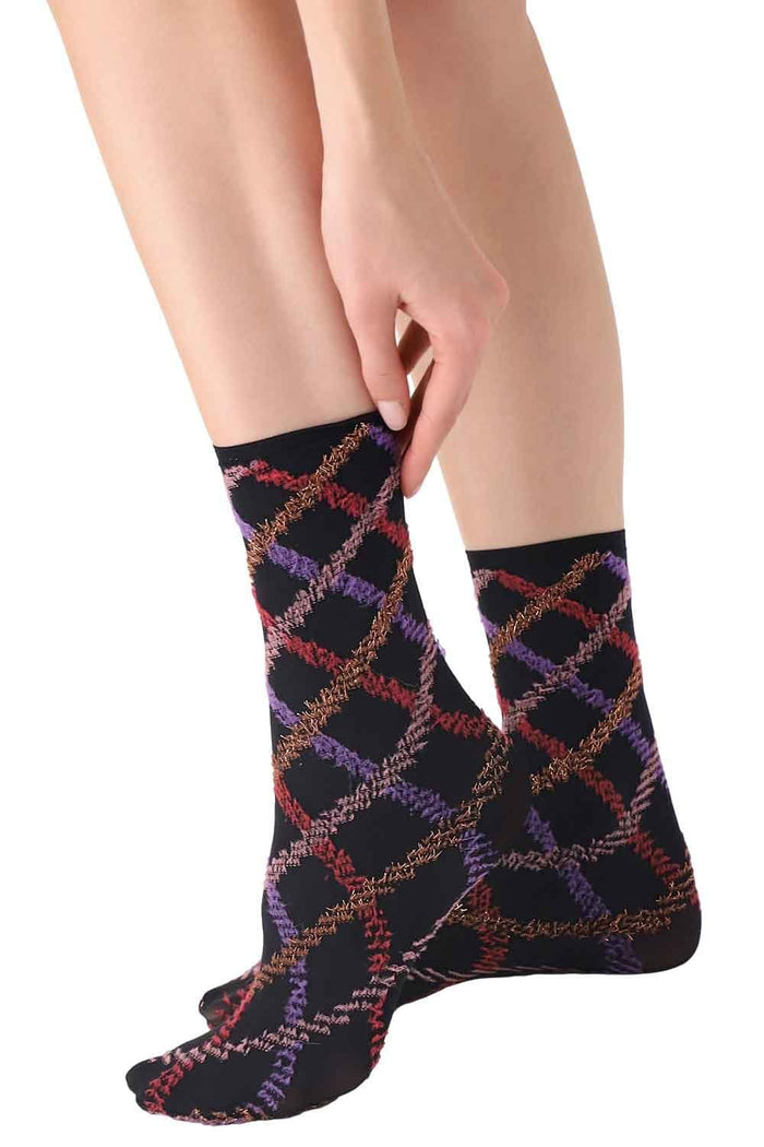 Person wearing a black sock with colorful tartan  pattern on a white background