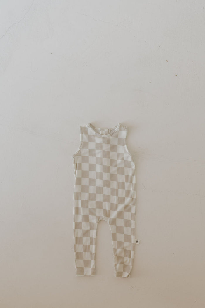 A beige and off-white checkered Harem Bamboo Romper by forever french baby is laid flat on a plain, light-colored surface.