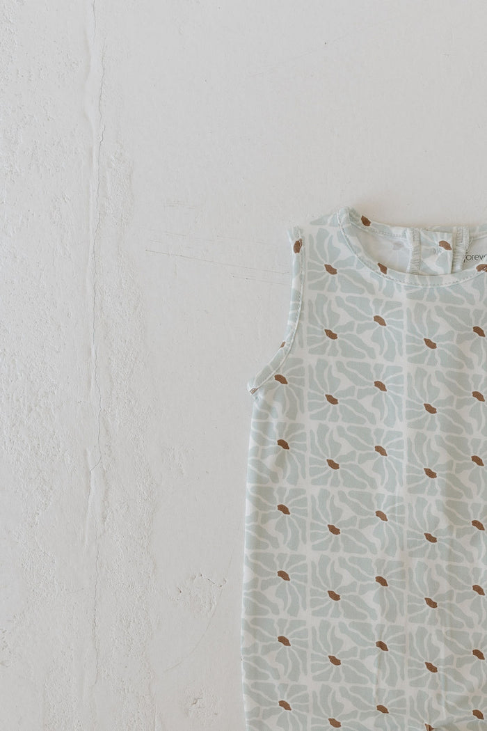 The Harem Bamboo Romper by forever french baby combines style and comfort with its breathable fabric, featuring a light blue and white floral pattern accented by small brown dots. Laid flat on an off-white surface, this sleeveless romper is perfect for any occasion.