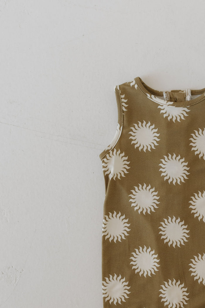 The Harem Bamboo Romper | Sol by forever french baby is partially displayed on a light neutral surface, showcasing its airy elegance with a beige background and white sun patterns in breathable bamboo fabric.