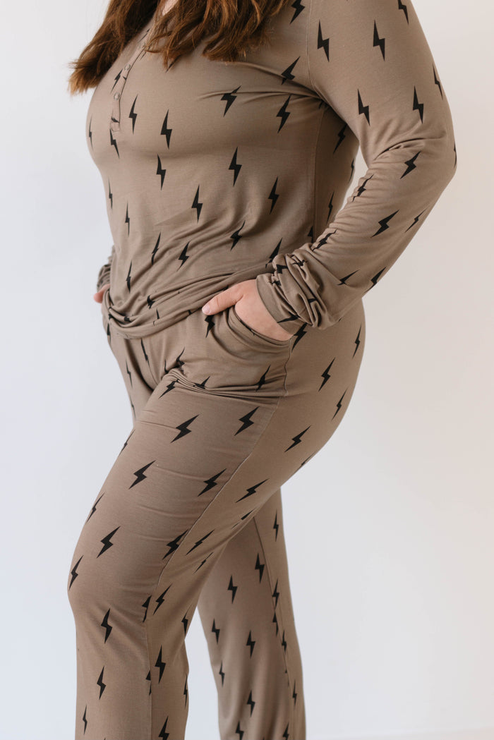 A person is wearing the Women's Bamboo Pajamas from forever french baby, featuring a matching set in brown with a black lightning bolt pattern. The set includes a long-sleeve top and pants made from breathable fabric. The person, with their hands in their pockets, is standing against a plain white background.