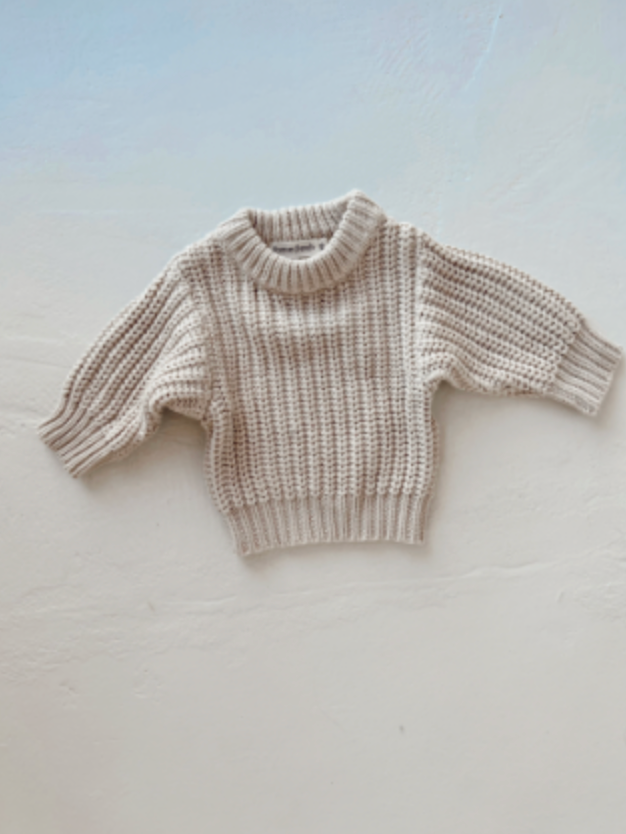 The Cream | Knit Sweater by forever french baby, a chunky-knit cotton design with long sleeves and ribbed neckline, cuffs, and hem, is displayed flat on a light background.